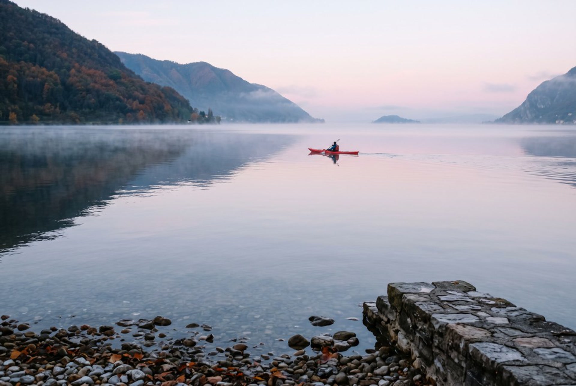 Kayak rosso all’alba sul lago, montagna e nebbia bassa